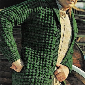 May include: A green knitted cardigan with a shawl collar and button closure. The cardigan has a textured stitch pattern.