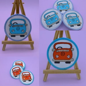 May include: Three embroidered iron-on patches featuring a cartoon car. The car is blue with white accents and a white steering wheel. The patches are displayed on a wooden easel.