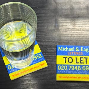 May include: A clear glass of water sits on a yellow and blue coaster. The coaster has the text "951 lettings biz" and "A family business est. since 1999". A second coaster reads "Michael & Eagle LETTINGS TO LET 020 7946 0951".
