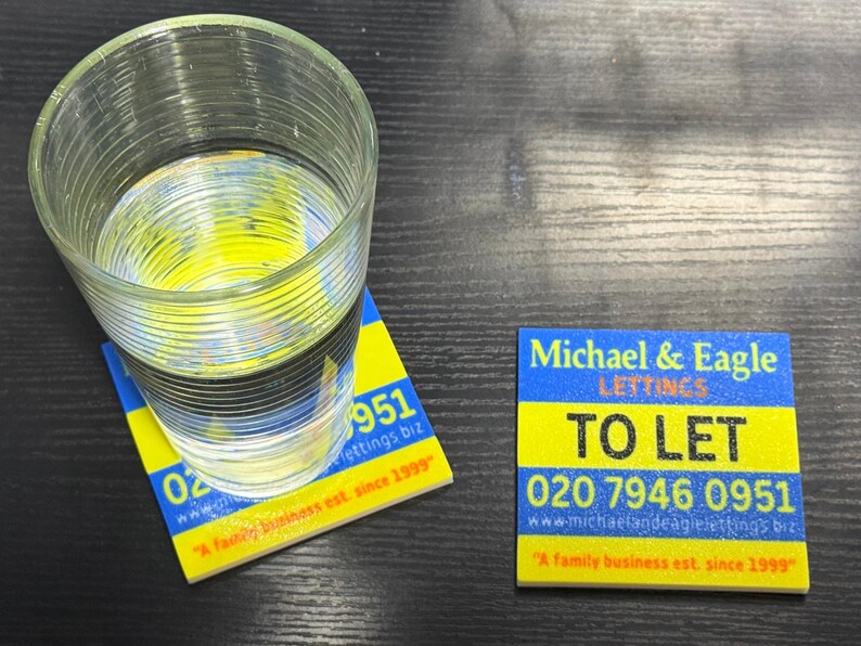 May include: A clear glass of water sits on a yellow and blue coaster. The coaster has the text "951 lettings biz" and "A family business est. since 1999". A second coaster reads "Michael & Eagle LETTINGS TO LET 020 7946 0951".