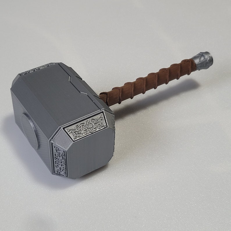 May include: A gray plastic replica of Thor's hammer, Mjolnir, with a brown leather-wrapped handle. The hammer head features intricate carvings.