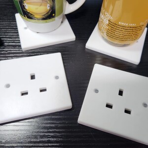 May include: Four white plastic electrical outlet covers with three prongs each. The covers are on a dark wood surface.