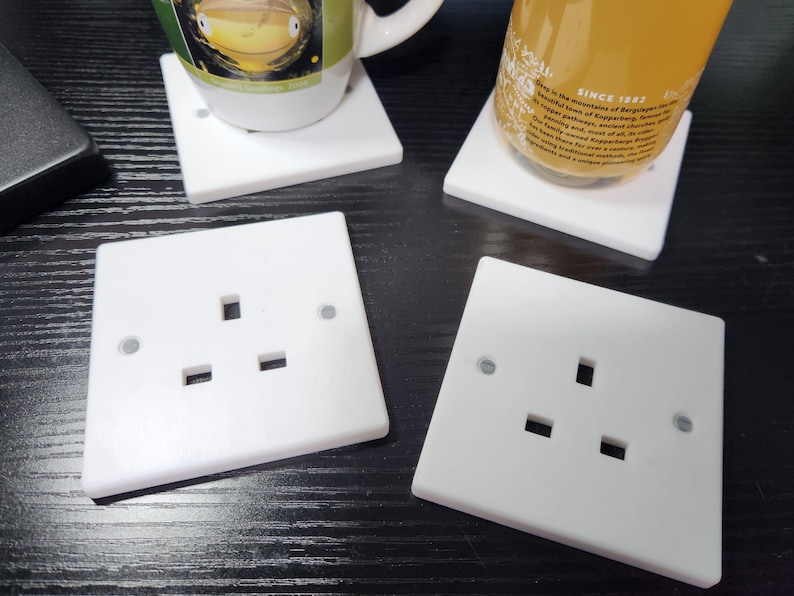 May include: Four white plastic electrical outlet covers with three prongs each. The covers are on a dark wood surface.