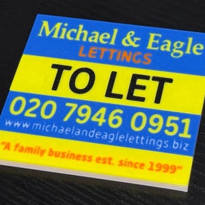 May include: A square sign with the text "Michael & Eagle LETTINGS TO LET" in blue and black. The sign also includes a phone number and website address, with the tagline "A family business est. since 1999".