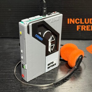 May include: A gray portable stereo cassette player with the brand name AIWA. The player has a black and gray design with the word "STEREO" in blue. Included are orange headphones with a silver band.