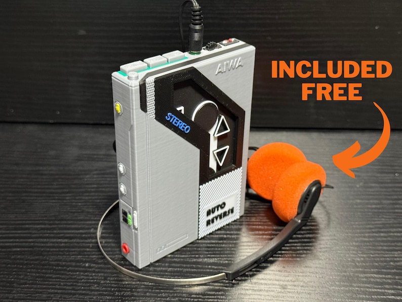 May include: A gray portable stereo cassette player with the brand name AIWA. The player has a black and gray design with the word "STEREO" in blue. Included are orange headphones with a silver band.