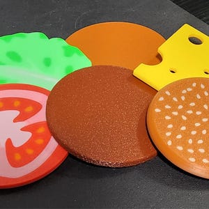 May include: A set of felt food items, including a tomato, lettuce, cheese, hamburger patty, and a sesame seed bun.