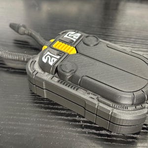 May include: A black and yellow device with two cylindrical tubes extending from the top. The device has a rectangular shape with rounded edges and a textured surface. The design includes yellow accents and white symbols.
