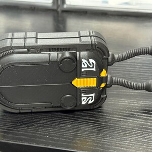 May include: A black, rectangular device with yellow and white accents. Two flexible, tube-like appendages extend from the top. The device has a textured surface and appears to be a piece of equipment or a model.