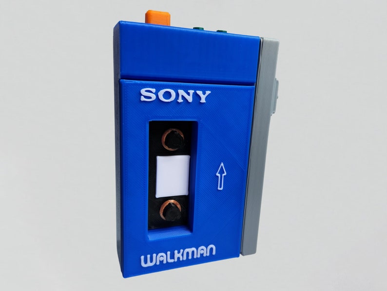 May include: A blue Sony Walkman cassette player with a white cassette tape inside. The player has a white label that says "WALKMAN" and a white label that says "SONY".