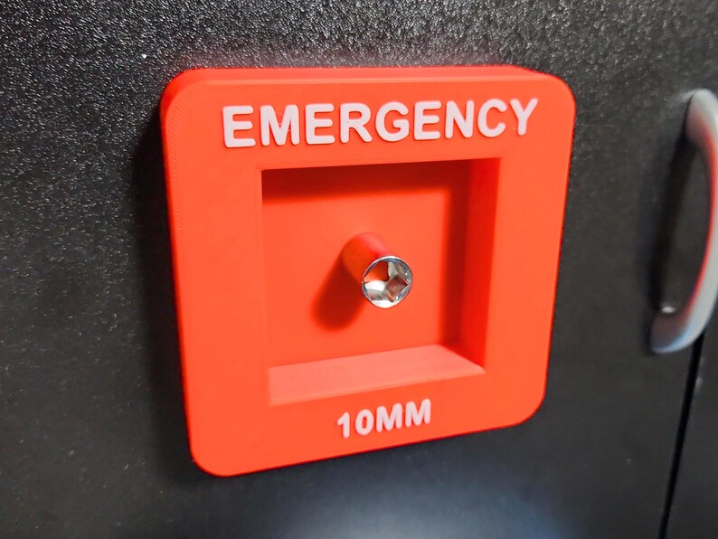 May include: Red plastic emergency access panel with the text "EMERGENCY" and "10MM" in white lettering. A silver socket wrench is visible in the center of the panel.