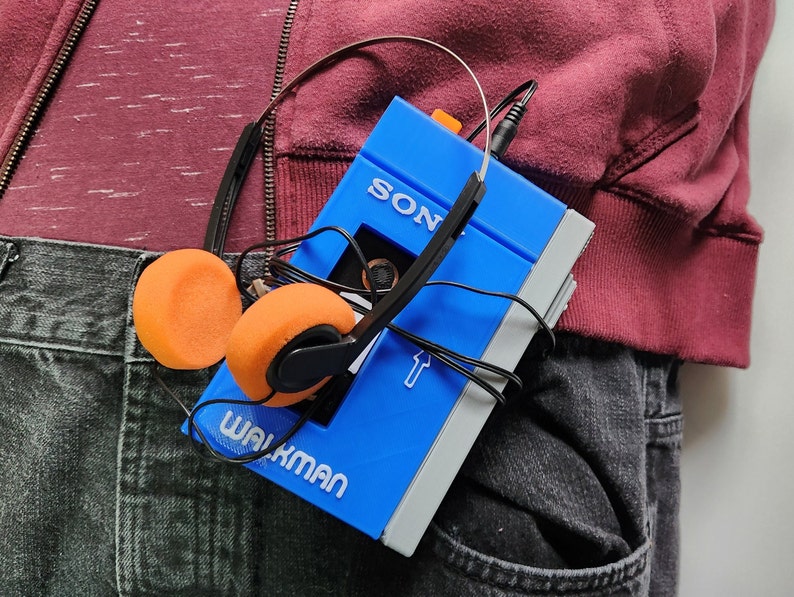 May include: A blue Sony Walkman cassette player with orange headphones. The Walkman is in a person's pocket.