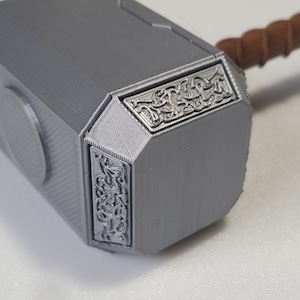 May include: A silver-colored 3D printed replica of Thor's hammer, Mjolnir, with intricate details and a brown handle.