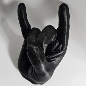 Puede incluir: Una escultura de mano impresa en 3D de color negro en forma de gesto de rock and roll.