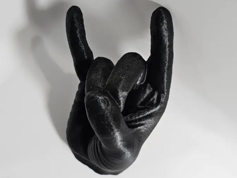 Puede incluir: Una escultura de mano impresa en 3D de color negro en forma de gesto de rock and roll.