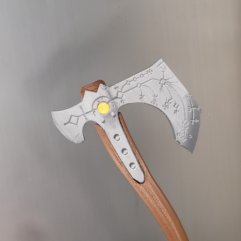 Op de afbeelding: Een zilveren bijl met een houten steel. De bijlkop heeft een decoratief ontwerp met een gele cirkel in het midden.