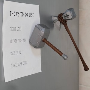 May include: A white to-do list on a refrigerator with the text "THOR'S TO DO LIST" at the top. The list includes the items "FIGHT LOKI", "CLEAN MJOLNIR", "BUY MEAD", and "TAKE JANE OUT". Two toy hammers are attached to the refrigerator with magnets.
