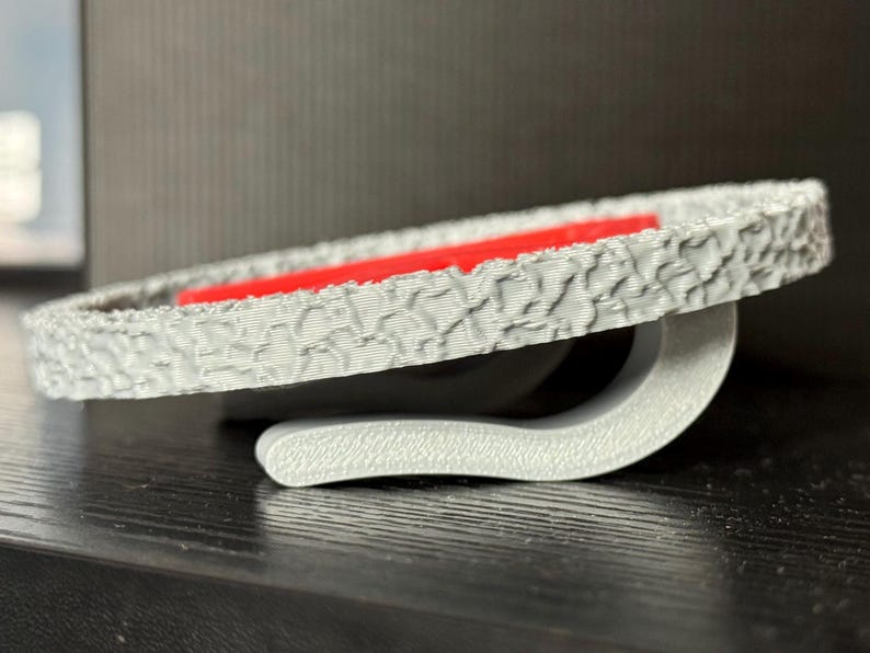 May include: A gray, textured, circular object with a red interior. The object has a curved, gray support. The design has a tire-like pattern around the edge. The object is on a dark surface.