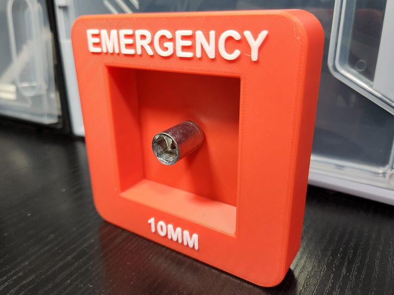 May include: Red plastic box with the word "EMERGENCY" in white lettering. The box has a cutout for a 10mm socket and the text "10MM" is printed below the cutout.