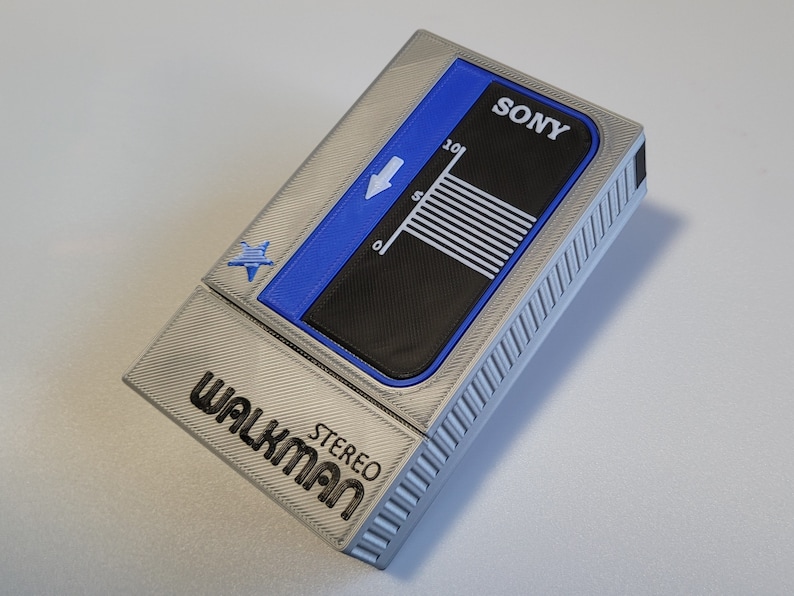 May include: A silver-colored Walkman stereo cassette player with blue and black accents. The top features the brand name "SONY" and a gauge. The word "WALKMAN STEREO" is printed on the front.