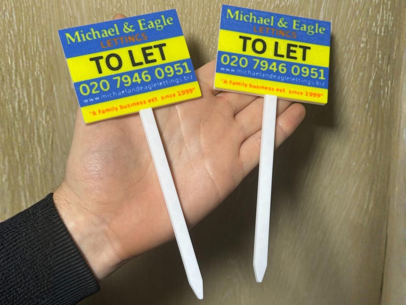 May include: Two "To Let" signs with white stakes. The signs have a blue and yellow background with the text "Michael & Eagle LETTINGS" and a phone number. The signs are for property rentals.