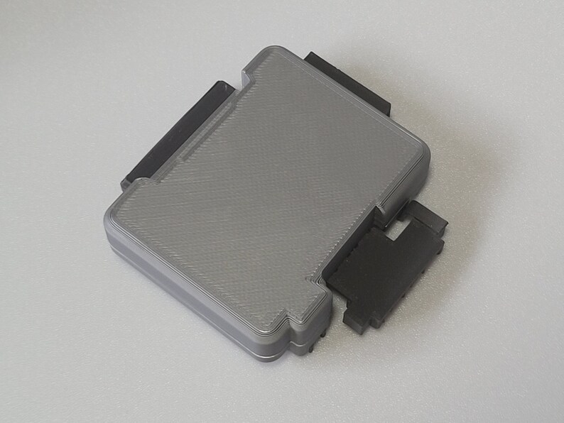 May include: A gray plastic case with a textured surface and black plastic hinges. The case is closed and the hinges are visible.