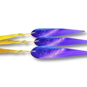 May include: Three purple and blue bookmarks with gold tassels. Each bookmark has a floral design and a gradient effect. The tassels are attached with gold-colored string.