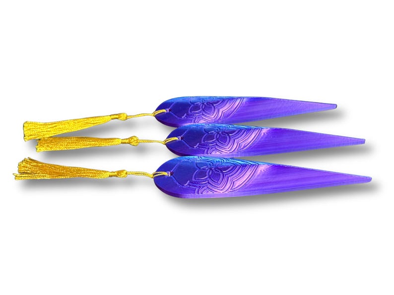May include: Three purple and blue bookmarks with gold tassels. Each bookmark has a floral design and a gradient effect. The tassels are attached with gold-colored string.