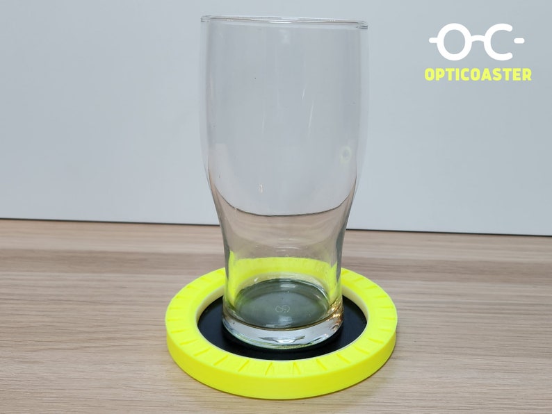 May include: A yellow circular coaster with a black center and a glass on top. The coaster has the text "OPTICOASTER" printed on it.