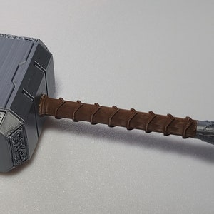 May include: A silver-colored hammer with a brown wooden handle. The hammer has intricate details and a textured surface.