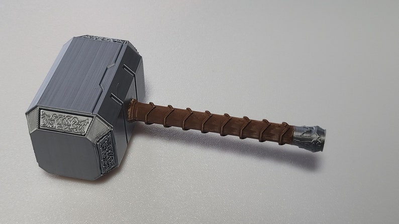 May include: A silver-colored hammer with a brown wooden handle. The hammer has intricate details and a textured surface.