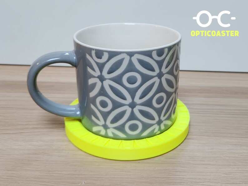 May include: A gray ceramic mug with a white geometric pattern sits on a bright yellow circular coaster. The coaster has a textured surface and a raised edge.
