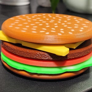 May include: A toy hamburger made of plastic with a brown bun, yellow cheese, red tomato, green lettuce, and a brown patty.