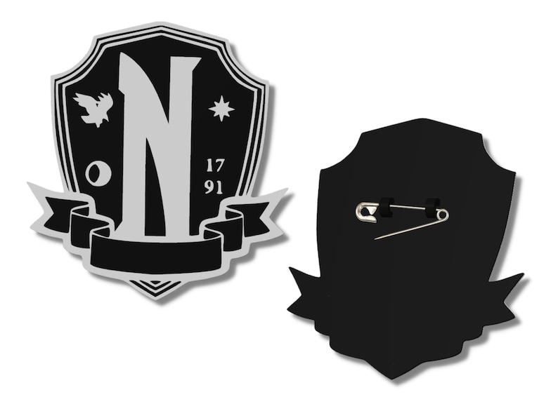 May include: Black and silver shield-shaped pin with a large letter N, a small bird, a star, and the numbers 17 and 91. The back of the pin has a safety pin.