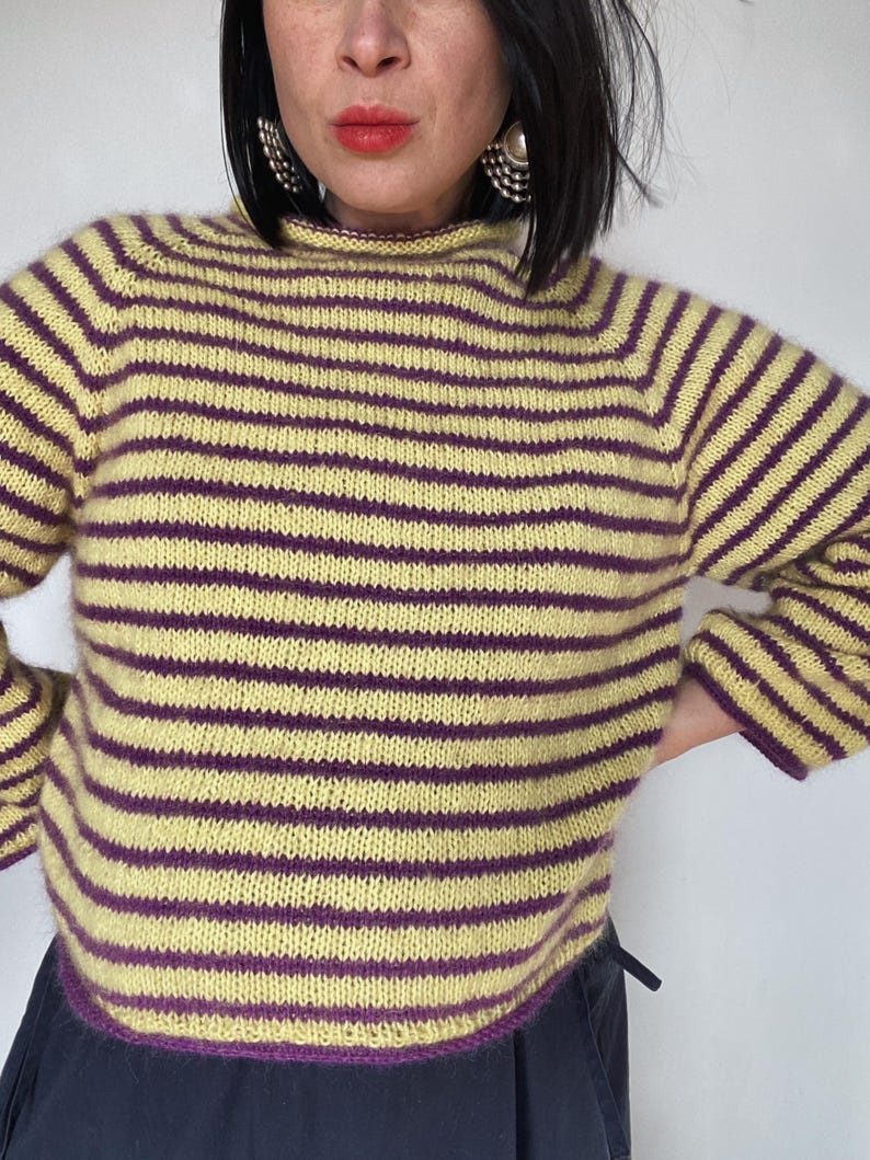 Puede incluir: Un su&eacute;ter a rayas amarillas y moradas. El su&eacute;ter tiene rayas horizontales en amarillo claro y morado oscuro. El cuello, los pu&ntilde;os y el dobladillo est&aacute;n acabados con un ribete morado. Es un estilo de punto con mangas largas.