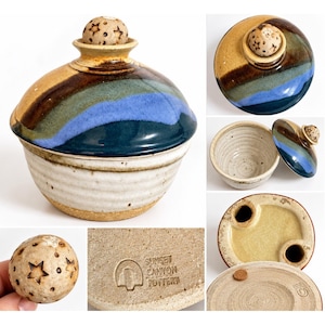 Op de afbeelding: Een keramische pot met deksel, beige basis en een blauw, groen en bruin geglazuurd deksel. Het deksel heeft een bolvormige knop met steruitsparingen. De onderkant is gestempeld met de tekst SUNSET CANYON POTTERY.