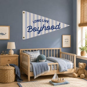 Puede incluir: Un banderín de pared triangular con rayas verticales de color azul claro y blanco, con el texto en azul oscuro LONG LIVE Boyhood impreso en el centro. El banderín incluye dos ojales metálicos en la base para fijarlo a la pared.
