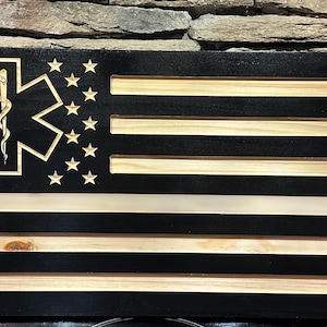Könnte beinhalten: Ein amerikanisches Flaggen-Design aus Holz mit schwarzem Hintergrund und Streifen aus Naturholz. Die Flagge zeigt ein Lebensstern-Symbol und Sterne in der oberen linken Ecke. Das Wort "SHORT" befindet sich in der unteren rechten Ecke.
