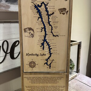 Puede incluir: Mapa enmarcado en madera del lago Kentucky y el lago Barkley, con los nombres de los arroyos y pueblos. El mapa está en un marco de madera con un contorno azul detallado de los lagos. El texto "Kentucky Lake" es visible.