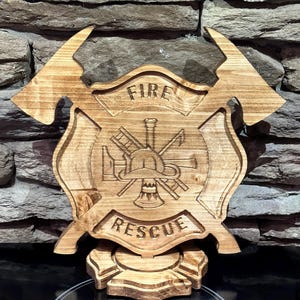 May include: A wooden firefighter emblem with the words "FIRE" and "RESCUE" carved into it. The emblem features a helmet, ladder, and other tools. The emblem is approximately 12 inches wide and 12 inches tall.