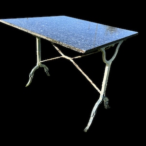 May include: A rectangular table featuring a dark, speckled granite top with a polished finish. The base is constructed from off-white, weathered metal with curved legs and a cross-brace support structure connecting the two sides of the frame.