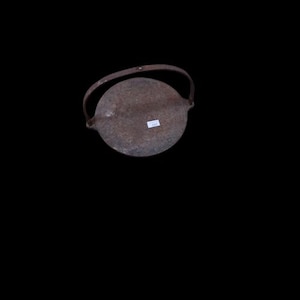Könnte beinhalten: Ein kreisförmiger, dunkelbrauner, verwitterter Metalldeckel mit einem gebogenen Griff an der Oberseite. Die Metalloberfläche weist Anzeichen von Oxidation und Textur auf, mit einem kleinen weißen rechteckigen Aufkleber mit schwarzem Text.