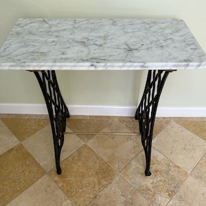May include: A white marble top table with a black cast iron base. The table has a simple design with a single shelf.