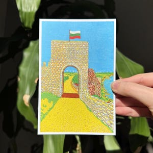 May include: A colorful illustration of a stone archway with a Bulgarian flag on top. The archway leads to a yellow path, with a blue sky and green landscape in the background. The artwork is on a white rectangular card.