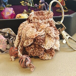 May include: A crocheted dice bag with brown and white yarn, featuring a key ring and a silver clasp. The bag has three brown and white beads attached to it.