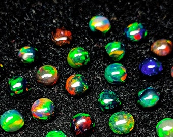 May include: A collection of iridescent opal cabochons in various shades of green, blue, and red. The cabochons are arranged in a circular pattern on a black background.