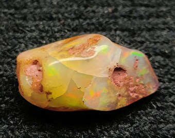 May include: A polished opal gemstone with a mix of colors, including yellow, orange, and hints of green and red. The opal has a rough, natural texture with a smooth, glossy surface. The gemstone is a unique, natural stone.