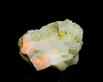 May include: A rough, white opal with green and orange inclusions. The opal is set in a matrix of dark green rock.