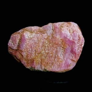 May include: A rough, pink ruby gemstone with a natural, irregular shape. The ruby has a deep pink colour with a slight shimmer.