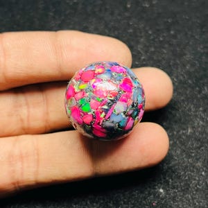 Puede incluir: Una esfera redonda e iridiscente hecha de pequeños trozos de ópalo de colores. La esfera tiene un diámetro de aproximadamente 2,5 cm y presenta una variedad de colores, incluyendo rosa, morado, verde y azul.